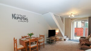 A living room with a dining table, chairs, a TV, and a staircase. - Jasmine Cottage (Richmond)