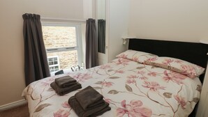 A bedroom with a bed, floral bedding, a window with curtains, and a view of a stone wall. - Jasmine Cottage (Richmond)