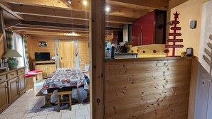A wooden interior with a dining table, chairs, a television, and a red cabinet. - Cozy Chalet by the Stream: Terrace, BBQ, Near Skiing & Cycling Paths, Pet Friendly (Vagney)