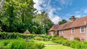 Une maison en briques avec un jardin bien entretenu, un chemin de pierres et un grand arbre en arrière-plan.