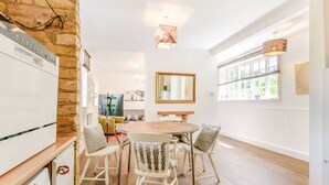 Une cuisine moderne avec un mur en briques, un coin repas avec une table ronde et quatre chaises, et une grande fenêtre avec des stores.