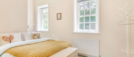 A bedroom with a bed, bedside table, dresser, windows, and a coat rack.