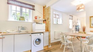 Une cuisine compacte équipée d’un lave-linge, un coin repas avec une table et des chaises, et un mur décoratif en pierre.