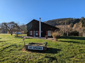 A rustic wooden cabin with a chimney, a sign reading "LES CAPUCINES," and a grassy field in the foreground. - Family-Friendly Chalet in Orchard with Modern Comforts & Spacious Terrace (Ban-sur-Meurthe-Clefcy)