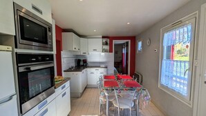 Une cuisine compacte dotée d’appareils électroménagers modernes, un coin repas avec une table et des chaises, et une fenêtre donnant sur un espace verdoyant.
