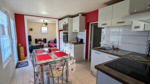 Une cuisine compacte avec des meubles blancs, une cuisinière noire et un coin repas comprenant une table en verre et des chaises à motifs floraux.
