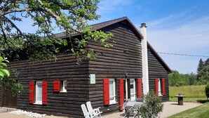 Une cabane en rondins avec des volets rouges, une cheminée et un espace salon extérieur.