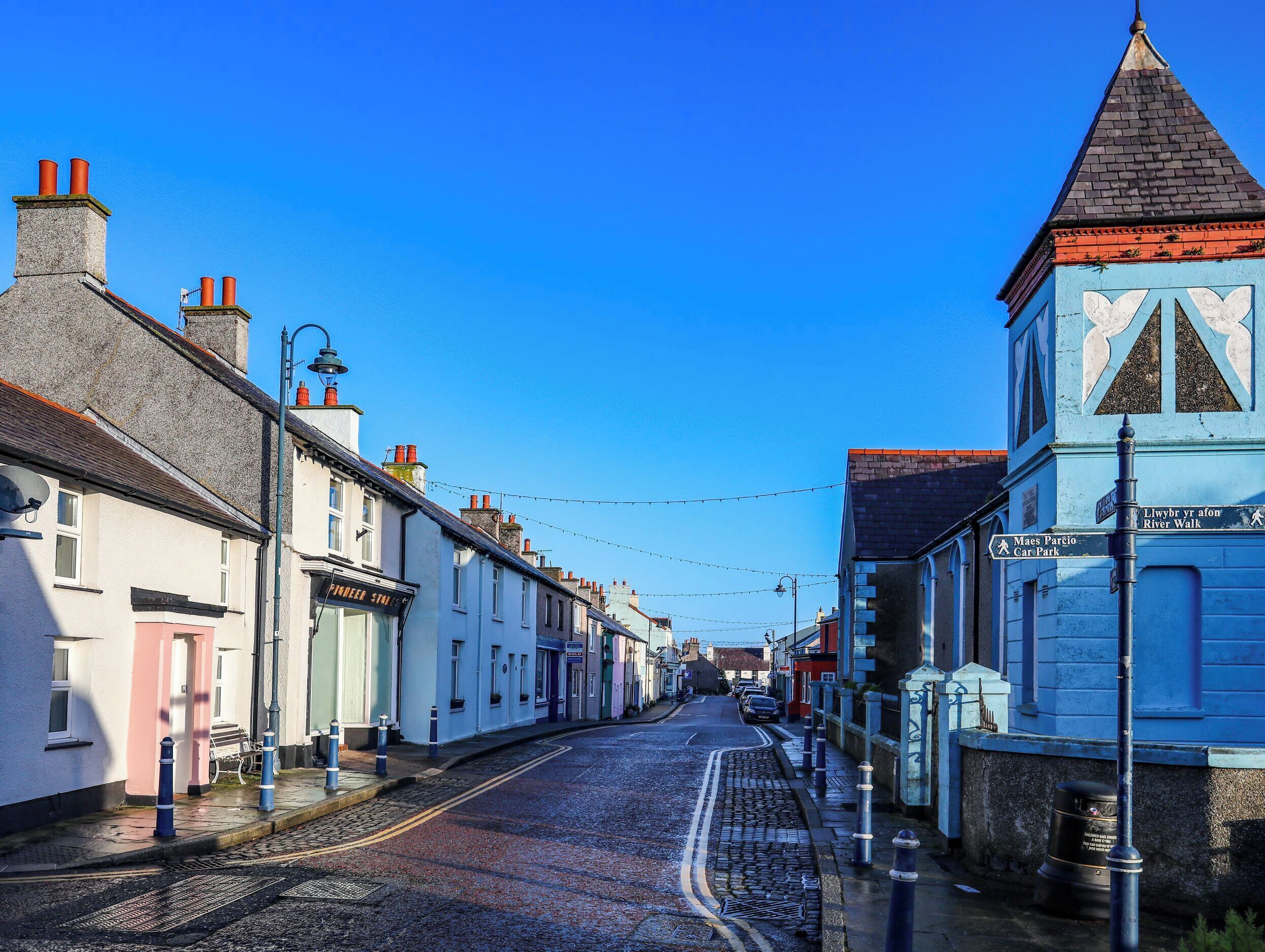 A street with buildings, a cobblestone road, bollards, and a signpost.