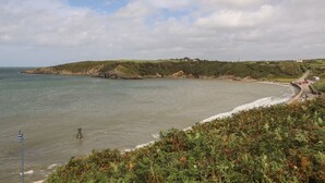 Een kustlandschap met een strand, heuvels begroeid met gras en een heldere lucht.