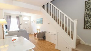 Un salon moderne avec un canapé blanc, une table à manger avec des chaises et un escalier doté d’une rampe blanche.