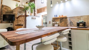 A modern kitchen with a wooden table, bar stools, and pendant lighting. - Elvan Cottage (Liskeard)