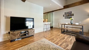Un soggiorno moderno con una TV a schermo piatto, pavimento in legno, un tappeto decorato e un'area pranzo con tavolo e sedie.