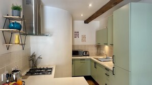 Una cucina moderna con piano cottura a gas, forno a microonde e mobili verdi. Ci sono ciotole di frutta sul bancone e una pianta su uno scaffale.