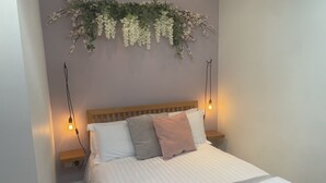 Un letto ben rifatto con una coperta a righe, due cuscini e una pianta decorativa sospesa sopra.