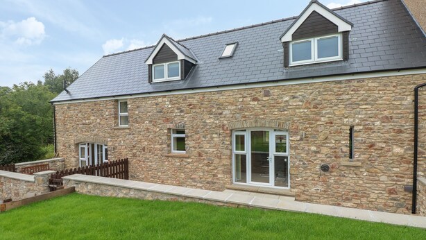 A stone house with a sloped roof, a fenced yard, and a well-maintained lawn. - Woodpecker Barn (Pontyclun)