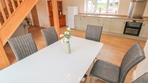 A modern kitchen with a central island, wooden staircase, and a dining area with grey upholstered chairs. - Woodpecker Barn (Pontyclun)