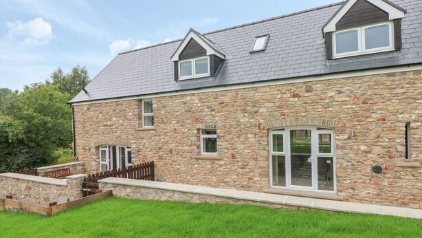 A stone house with a sloped roof, multiple windows, and a well-maintained lawn. - Nuthatch Barn (Pontyclun)