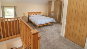 A bedroom with a wooden bed, a wardrobe, a bedside table with lamps, and a window with curtains. - Nuthatch Barn (Pontyclun)