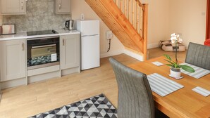 A modern kitchen with a built-in oven, a white refrigerator, and a wooden staircase. - Nuthatch Barn (Pontyclun)