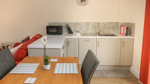 A compact kitchen with a microwave, sink, and a clock on the wall. - Nuthatch Barn (Pontyclun)