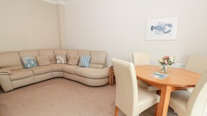 A living room with a beige sectional sofa, a wooden dining table with four chairs, and a framed picture on the wall. - Huffin (Dartmouth)