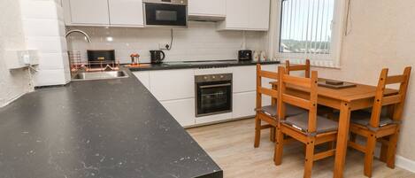 Una cocina moderna con armarios blancos, una encimera negra y una mesa de comedor de madera con sillas.