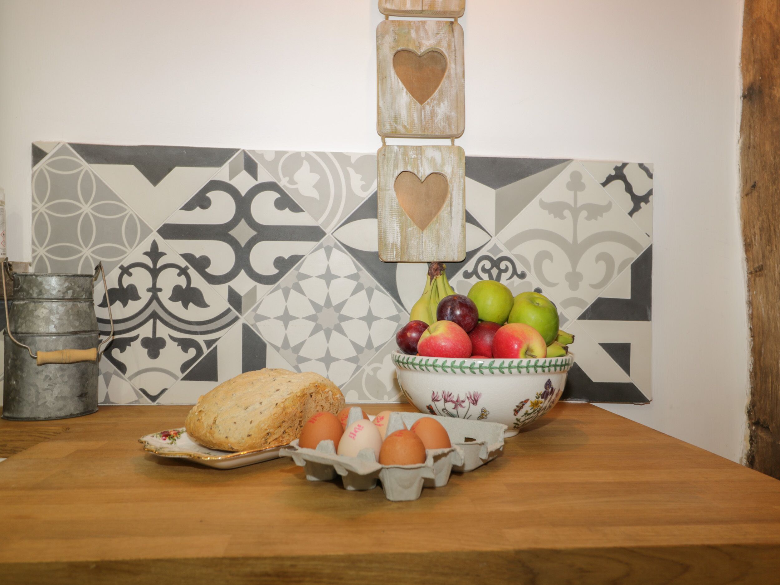 A kitchen counter with a bowl of fruit, eggs, and a loaf of bread.