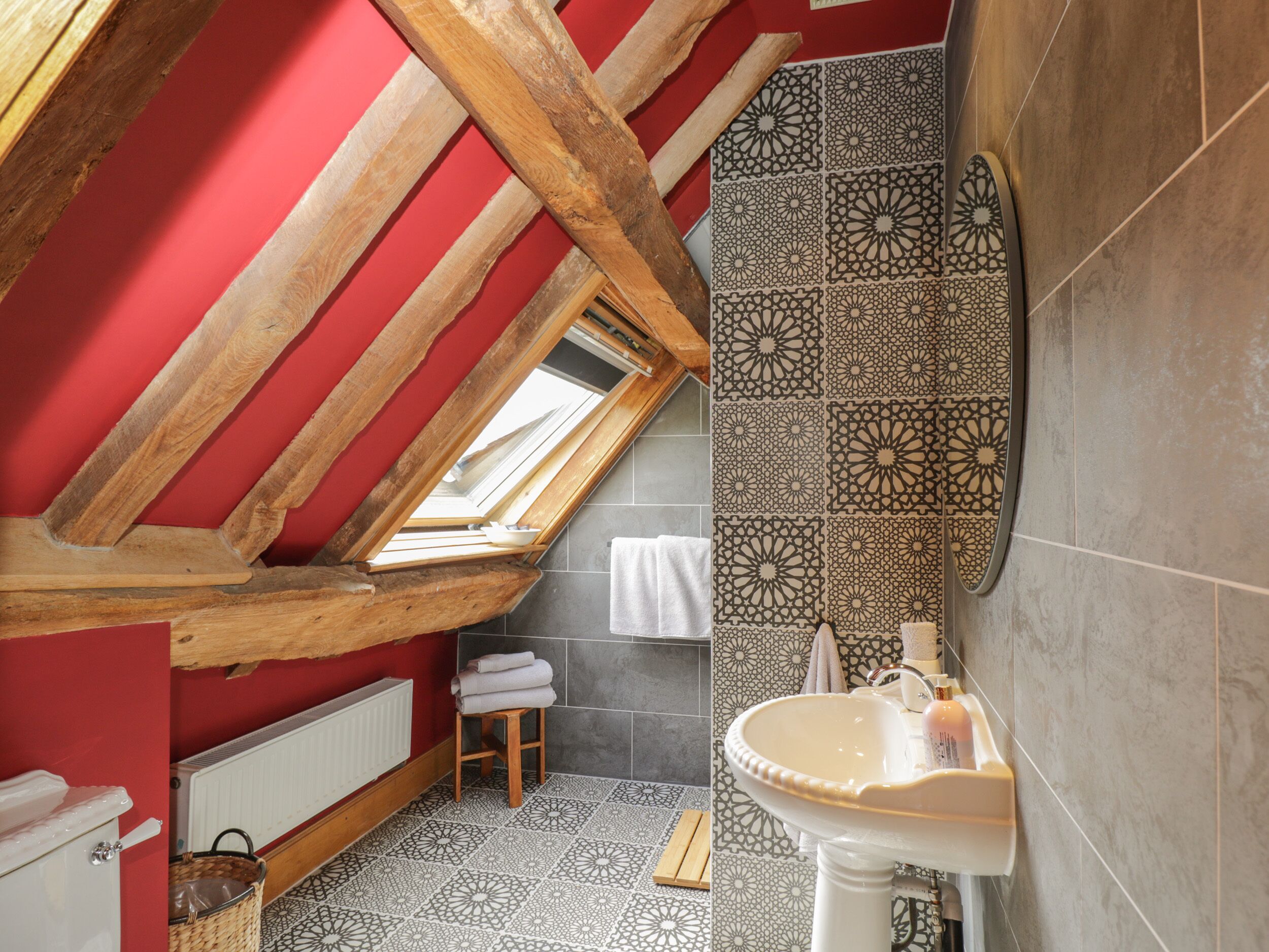 A bathroom with a sloped ceiling, a skylight, a sink, and patterned tiles.