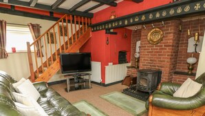 A living room with a fireplace, leather sofas, a TV, and a wooden staircase. - Caerau Farm House (Caersws)