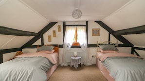 A bedroom with two beds, a small table, and a window with curtains. - Caerau Farm House (Caersws)