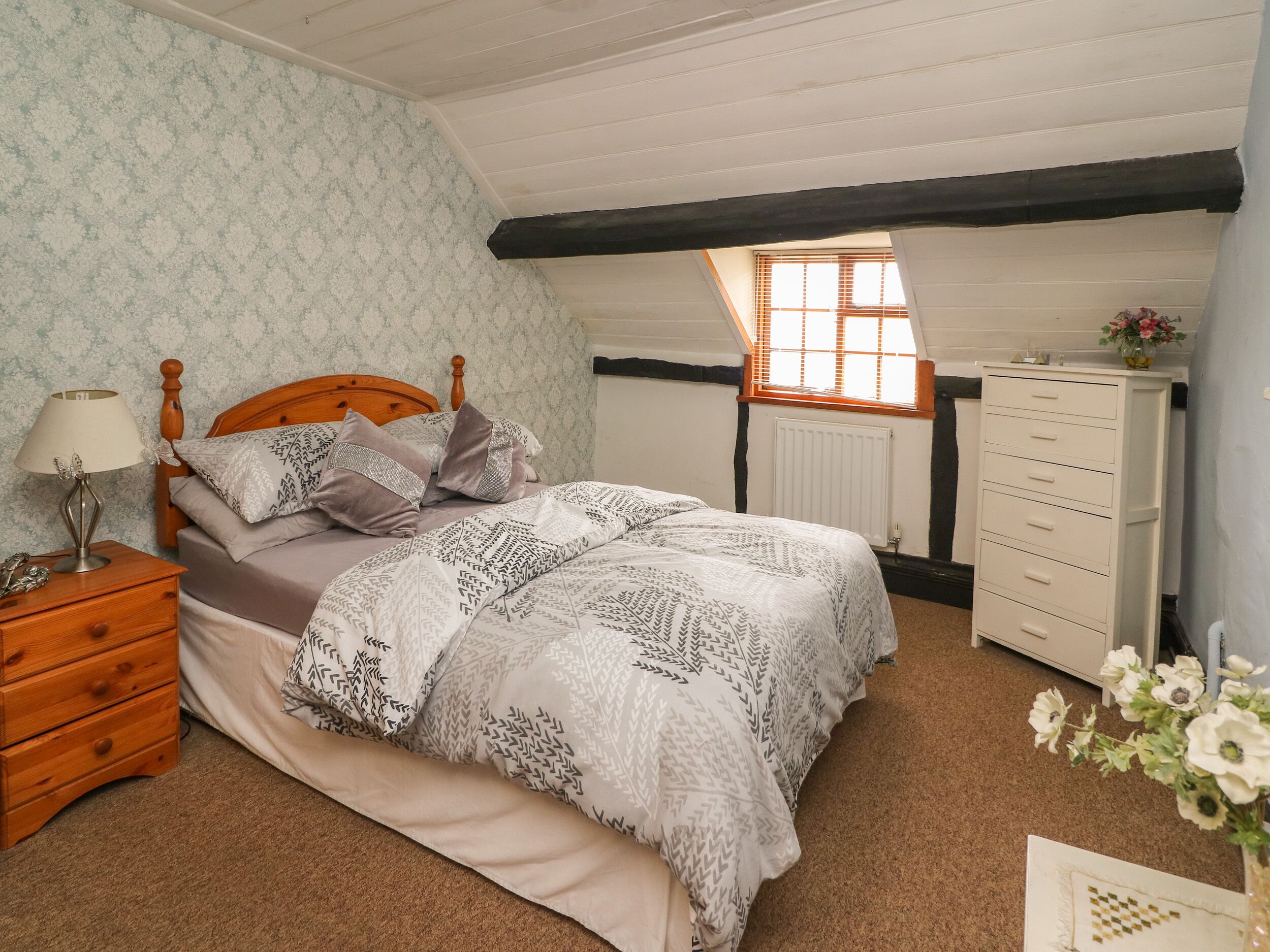 A bedroom with a wooden bed, a nightstand, a dresser, and a window with blinds.