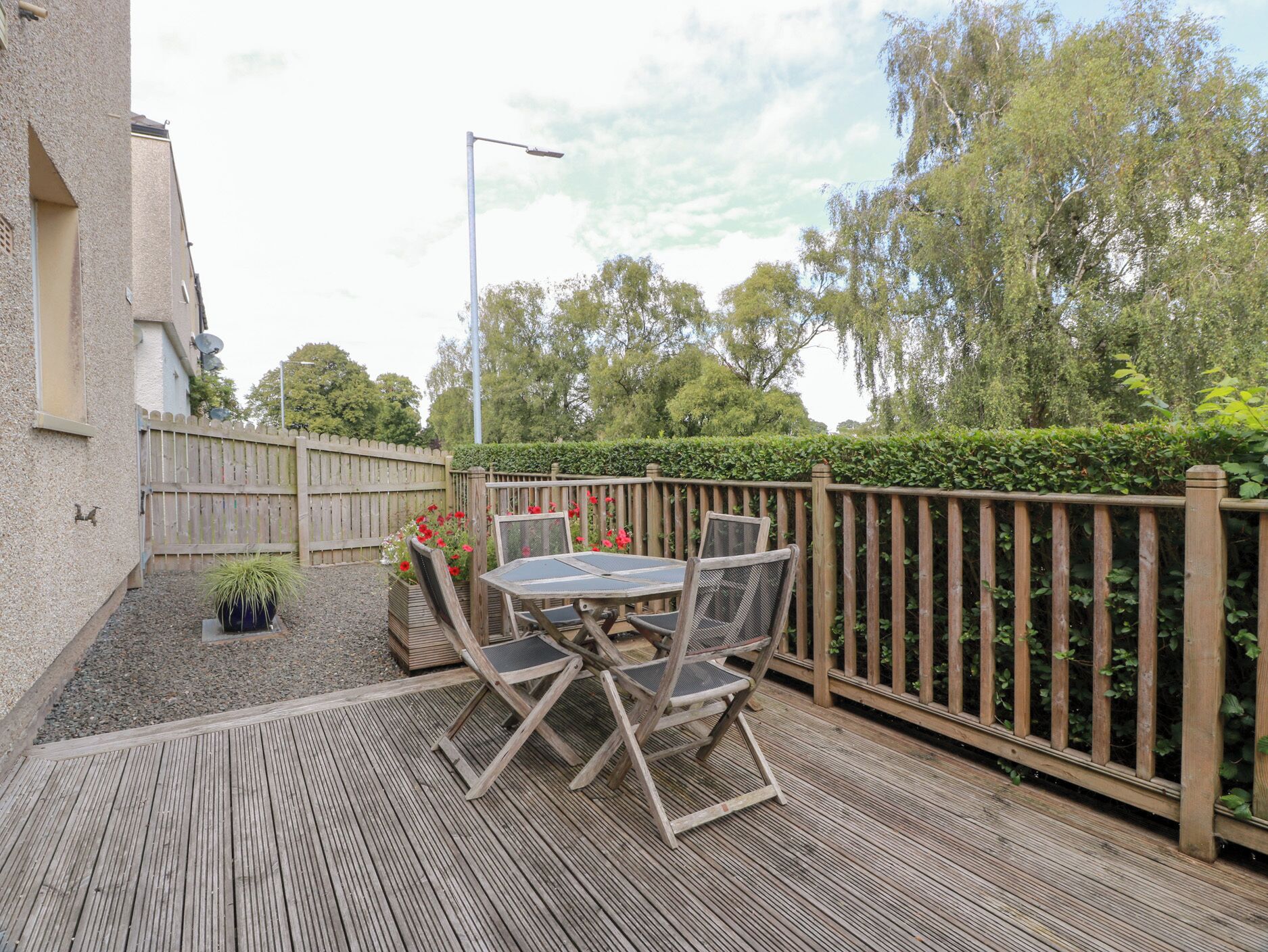 An outdoor patio with a table and chairs, a wooden fence, and a potted plant.