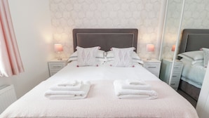 Un lit bien fait, avec deux piles de serviettes pliées, une tête de lit sombre et un mur orné d’un motif.