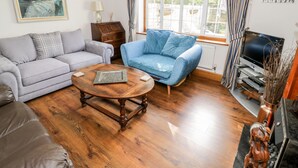 Un salon avec un canapé gris, un fauteuil bleu, une table basse en bois et un téléviseur posé sur un meuble.