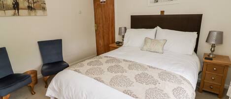 A bedroom with a large bed, two bedside tables, a chair, and a door with a fire action sign.