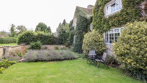 Un jardin avec une pelouse, une table et des chaises, et un bâtiment partiellement recouvert de lierre.