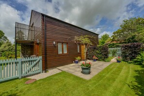 Une maison moderne en bois, dotée d’un balcon, de fondations en pierre et d’une pelouse bien entretenue.