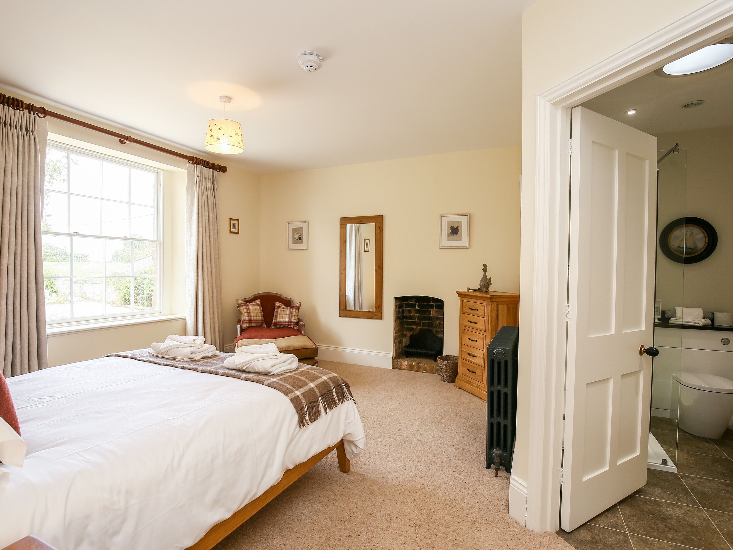 A bedroom with a large bed, a fireplace, a mirror, and a door leading to a bathroom.