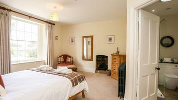 A bedroom with a large bed, a fireplace, a mirror, and a door leading to a bathroom.