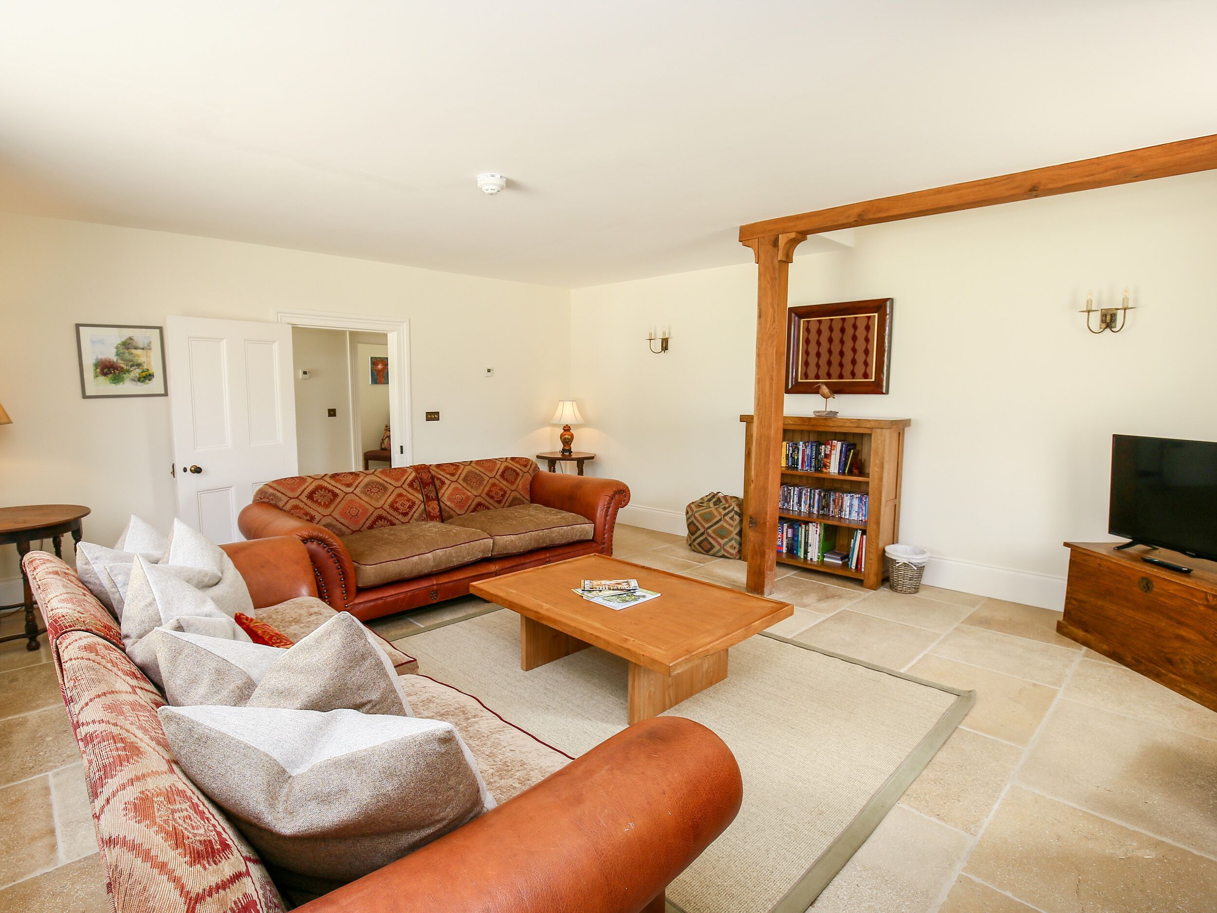 A living room with a sofa, coffee table, and a television. There is a bookshelf and a door leading to another room.