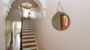 A staircase with white walls and a patterned floor, leading to a room with a wooden door and a hanging mirror. - Hawthorn House (Pembroke)
