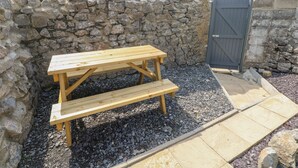 A wooden picnic table with benches in a garden area with a stone wall and a gate. - Hawthorn House (Pembroke)