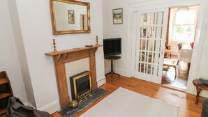 A living room with a fireplace, a television, and a door leading to another room. - Hawthorn House (Pembroke)