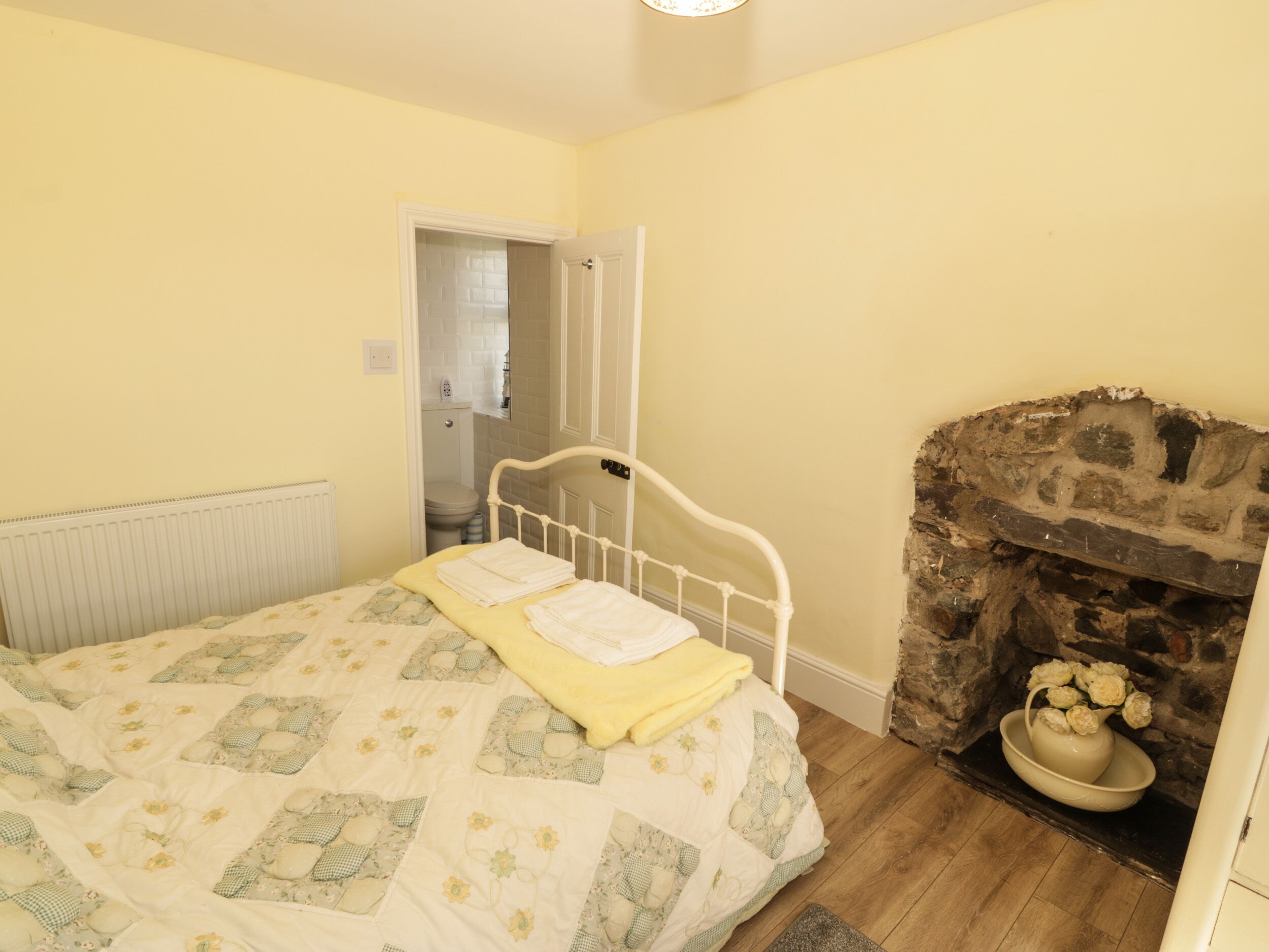 Een slaapkamer met een bed, een stenen openhaard en een deur naar een badkamer.