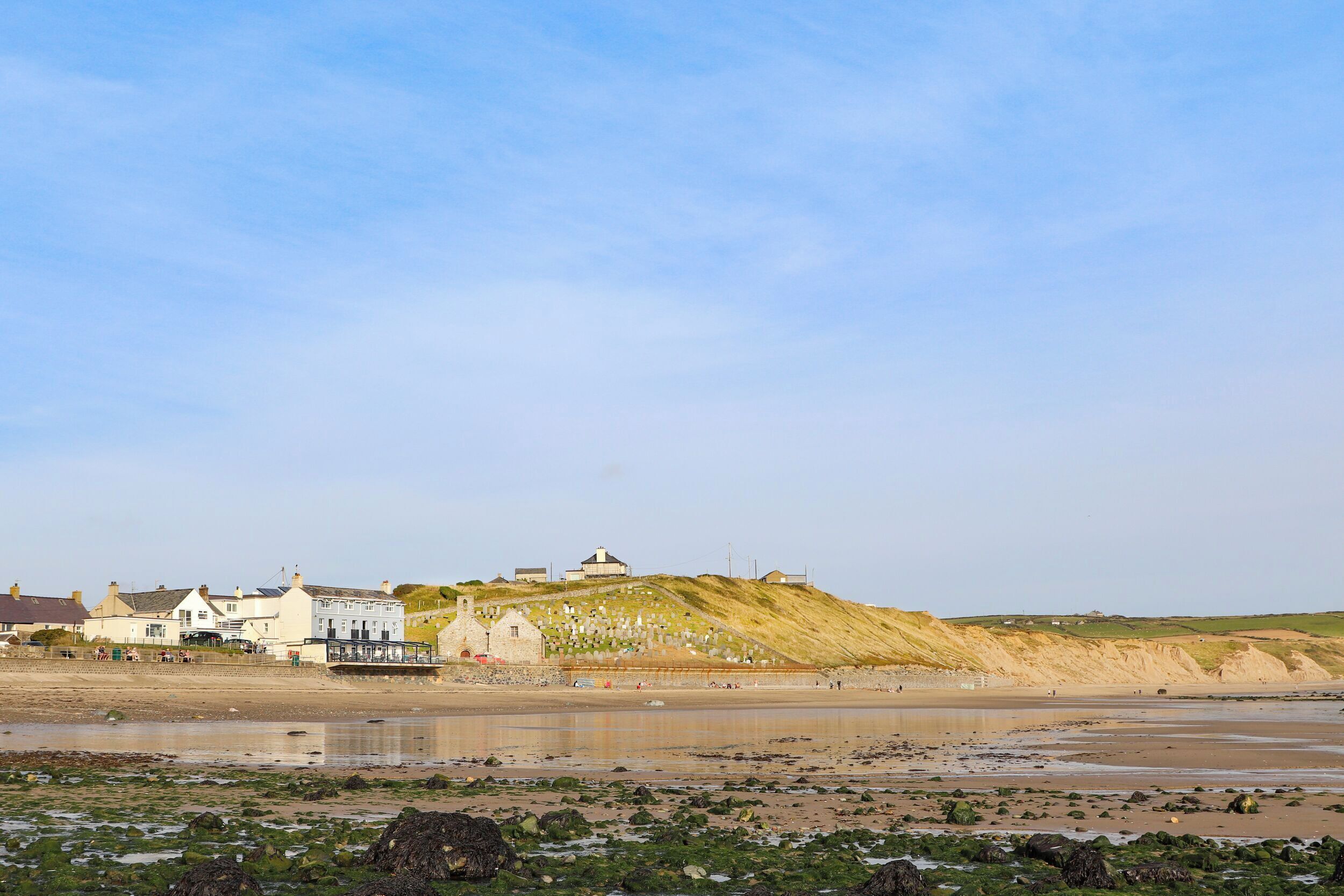 Un bâtiment situé sur la côte, doté d’un phare, et qui se trouve sur une plage de sable avec des rochers au premier plan.