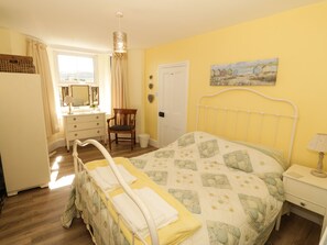 A bedroom with a bed, a chair, a dresser, a mirror, a door, and a painting on the wall. - Bryn Ffynnon (Pwllheli)
