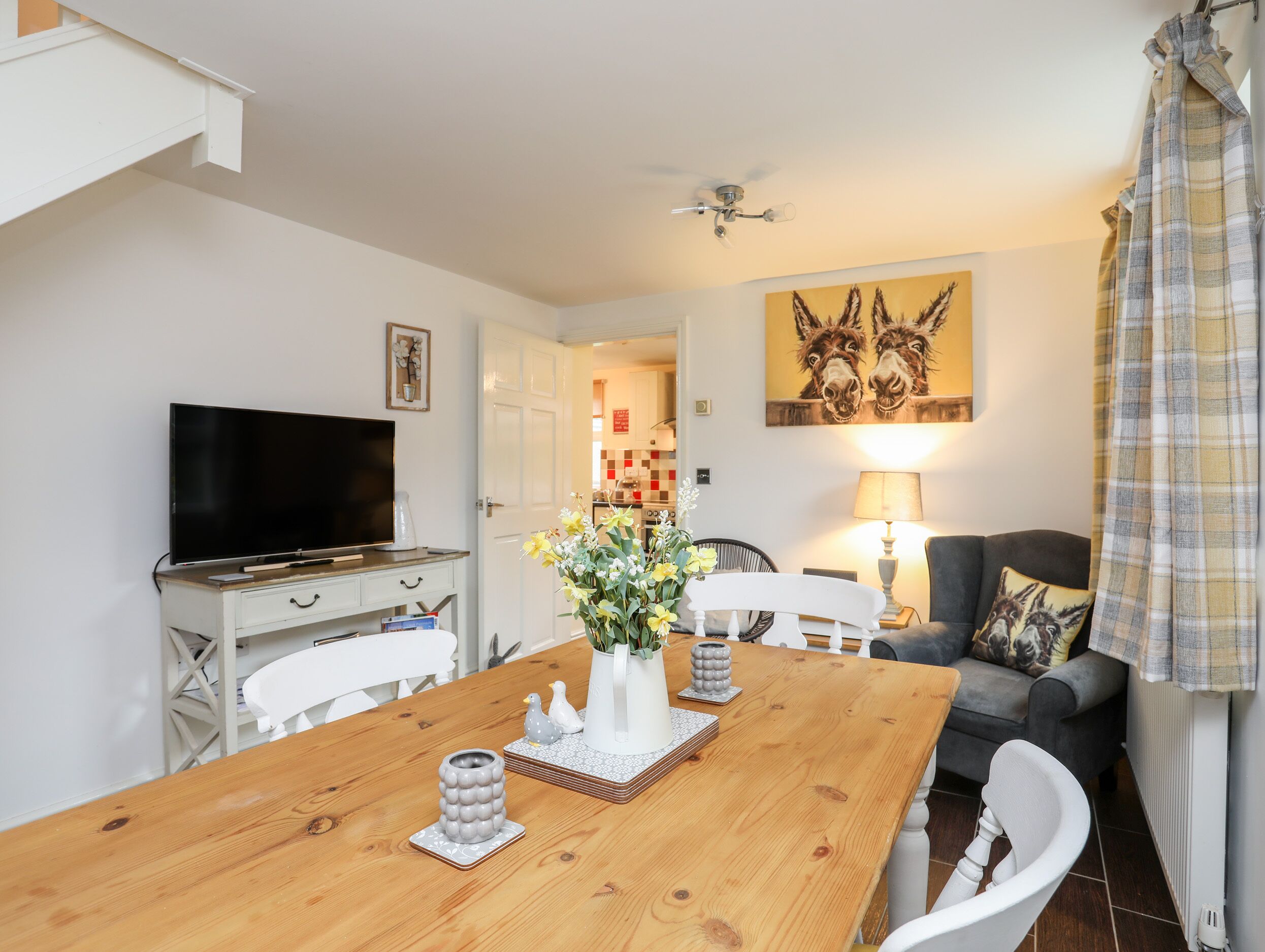 A dining area with a wooden table, chairs, a television, and a painting of donkeys on the wall.