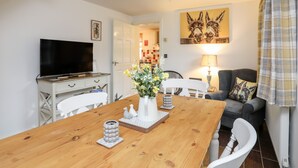 A dining area with a wooden table, chairs, a television, and a painting of donkeys on the wall. - Bwthyn Defaid (Pwllheli)