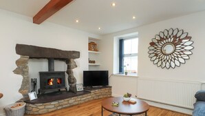 A living room with a stone fireplace, a television, a round coffee table, and a decorative mirror on the wall. - Bwthyn Defaid (Pwllheli)