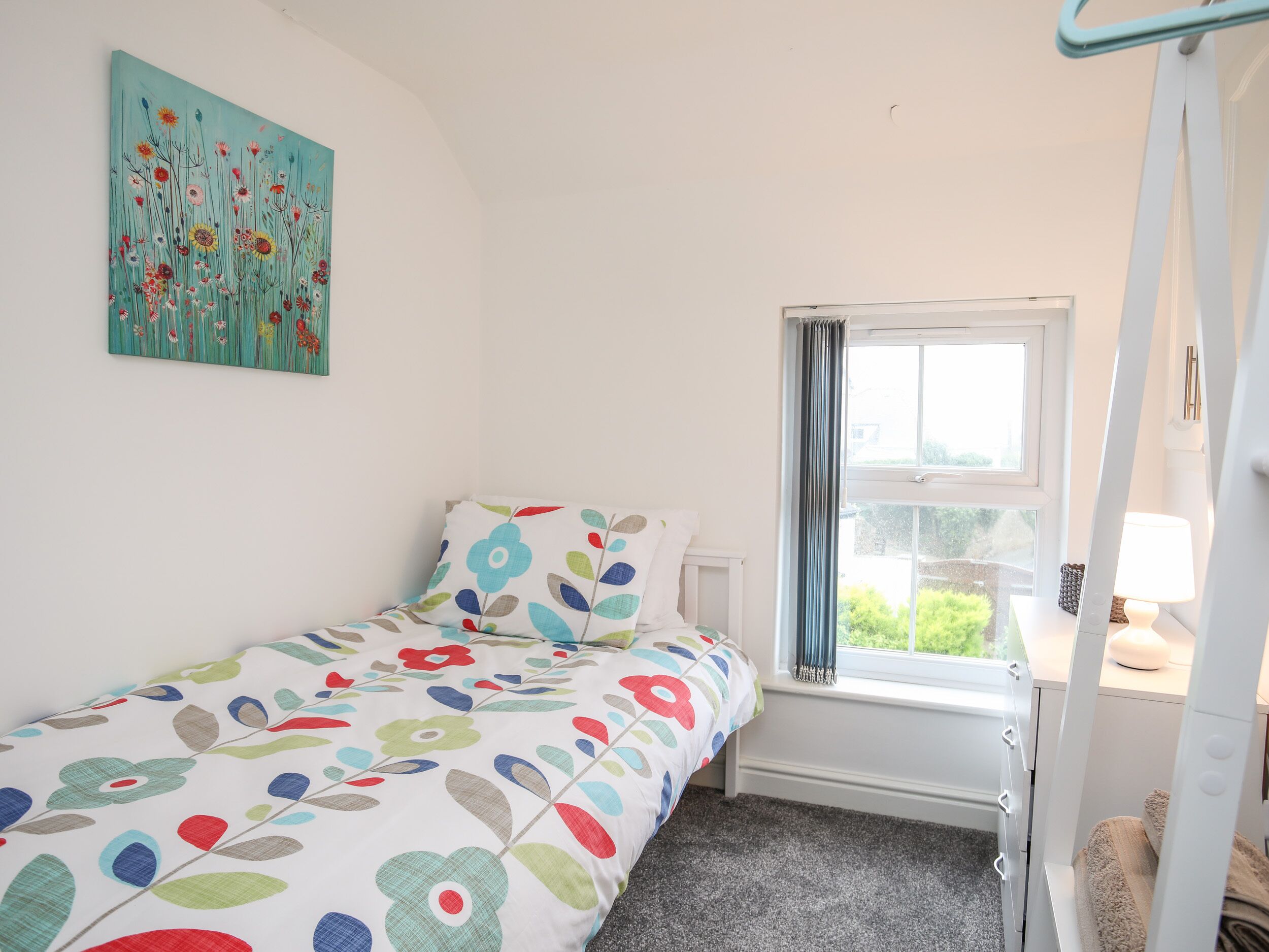 A bedroom with a bed, a window with curtains, a radiator, and a painting on the wall.